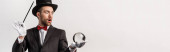 panoramatický záběr šokovaného kouzelníka držícího hůlku a magickou kouli, izolovaný na šedi