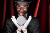 děsivý úsměv kouzelník drží magický míč v cirkusu s červenými závěsy