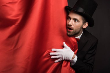 handsome emotional magician in suit and hat in circus with red curtains clipart