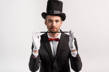young magician in suit and hat holding wand, isolated on grey clipart