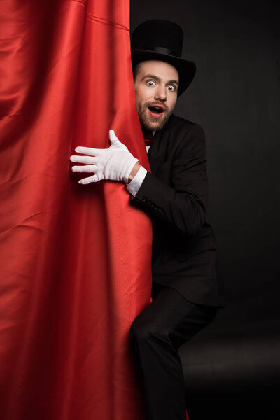 surprised magician in suit and hat in circus with red curtains