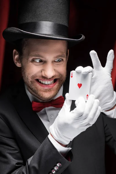 scary smiling magician holding playing cards in circus with red curtains
