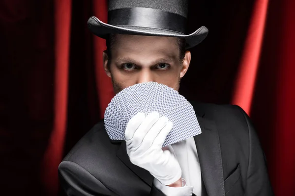 戴帽子的魔术师拿着红幕马戏团里的扑克牌 — 图库照片