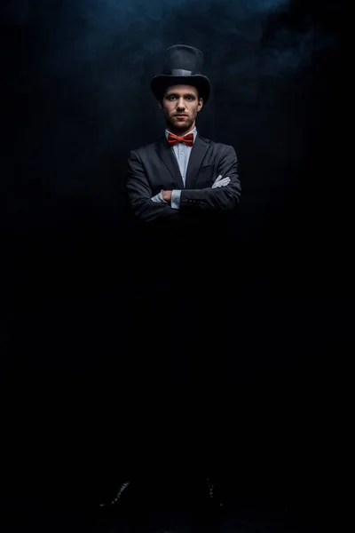 スーツ姿の魔術師と闇の煙室で腕を組んで立つ帽子 — ストック写真