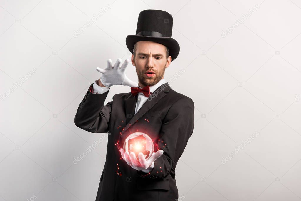 concentrated magician holding red magic ball, isolated on grey
