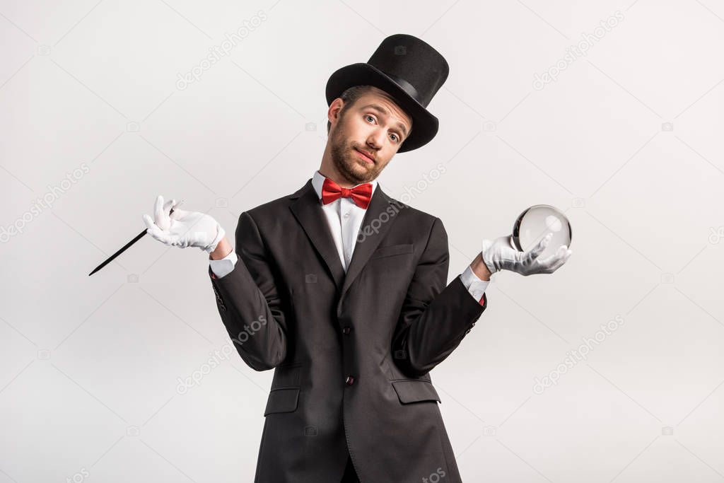 magician with shrug gesture holding wand and magic ball, isolated on grey