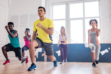 Low angle view of handsome trainer performing zumba with multiethnic dancers in dance studio clipart