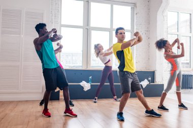 Young multicultural zumba dancers exercising movements in dance studio  clipart