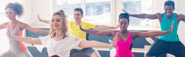 Dans stüdyosunda zumba yapan gülümseyen çoklu etnik dansçıların panoramik çekimi.