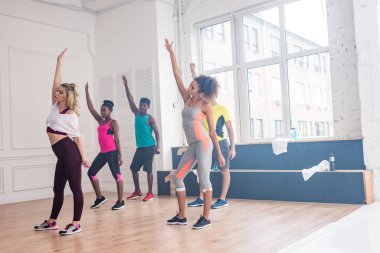 Dans stüdyosunda elleri havada zumba çalışan antrenör ve çok ırklı dansçılar.