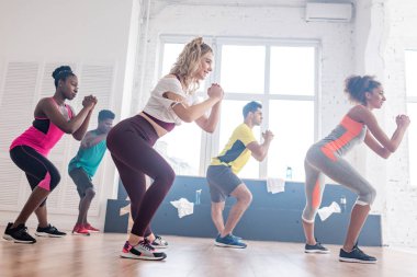Side view of smiling multiethnic dancers warming up before practicing zumba in studio clipart