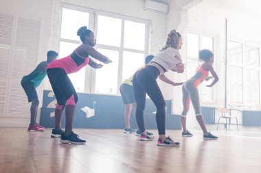 Dans stüdyosunda zumba hareketleri eğiten genç çok kültürlü dansçıların yan görüntüsü