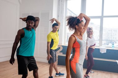 Güzel Afrikalı Amerikan zumba eğitmeninin yan görüntüsü dans stüdyosunda çok kültürlü dansçılarla hareketler yapıyor.