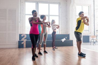 Dans stüdyosunda çok ırklı dansçılarla zumba hareketleri yapan yakışıklı antrenörlerin yan görünüşü
