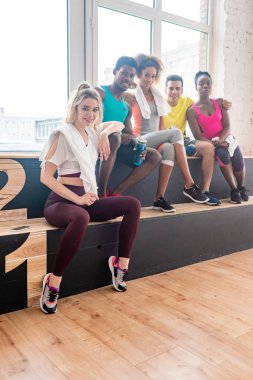 Young multicultural zumba dancers smiling at camera while resting in dance studio clipart