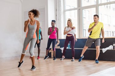 Güzel Afrikalı Amerikalı antrenör, dumanlı dans stüdyosunda çok kültürlü dansçılarla zumba hareketleri yapıyor.