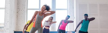 Afrika kökenli Amerikalı eğitmenin panoramik çekimi ve dans stüdyosunda zumba yapan genç çoklu etnik dansçılar.