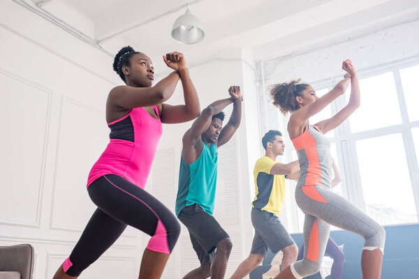 Low angle view of african american trainer learning with multicultural dancers movements of zumba in dance studio