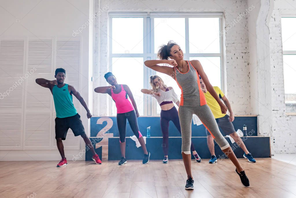 Smiling african american trainer performing zumba with multicultural dancers in dance studio