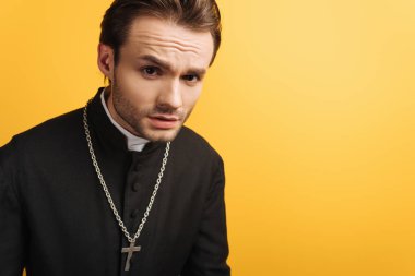 young thoughtful catholic priest looking at camera isolated on yellow
