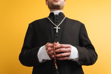 low angle view of catholic priest holding wooden rosary beads isolated on yellow