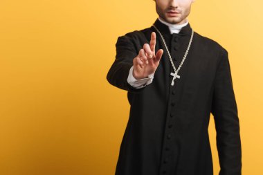 cropped view of catholic priest showing warning gesture isolated on yellow
