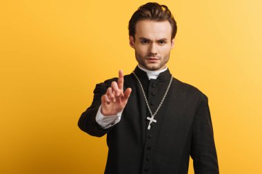 serious catholic priest showing warning gesture isolated on yellow