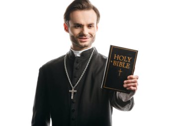 young catholic priest smiling while holding holy bible isolated on white clipart