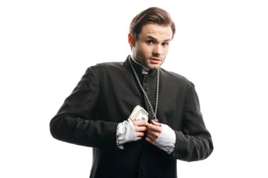scared catholic priest looking at camera while hiding money under cassock isolated on white clipart