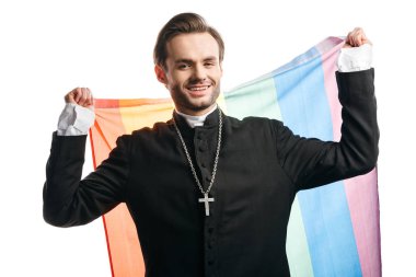 smiling catholic priest looking at camera while holding lgbt flag isolated on white clipart