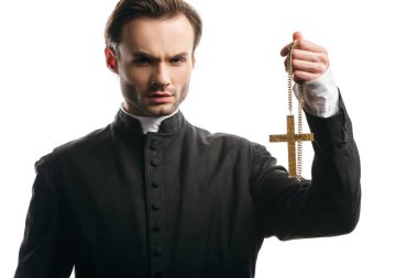 serious catholic priest holding golden cross while looking at camera isolated on white