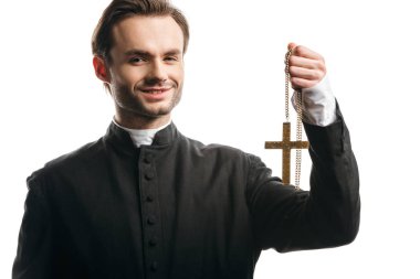 happy catholic priest holding golden cross while looking at camera isolated on white