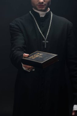 Kırpılmış Katolik rahibin kutsal İncil 'i elinde tuttuğu görüntüsü siyahların üzerinde izole bir şekilde uzanmış.