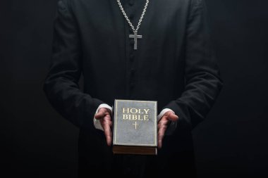 Kesilmiş Katolik papazın kutsal İncil 'i siyah üzerine izole ettiği görüntüsü.
