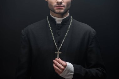 Siyah üzerine izole edilmiş gümüş haça dokunan katolik rahip görüntüsü.