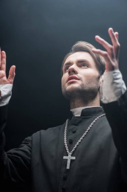 Genç, ciddi bir Katolik rahibin elleri havada dua edişinin düşük açılı görüntüsü.
