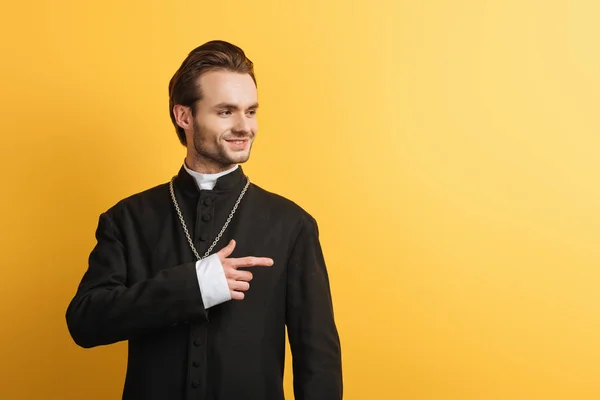 Smiling Catholic Priest Looking Away Pointing Finger Isolated Yellow — Stock Photo, Image