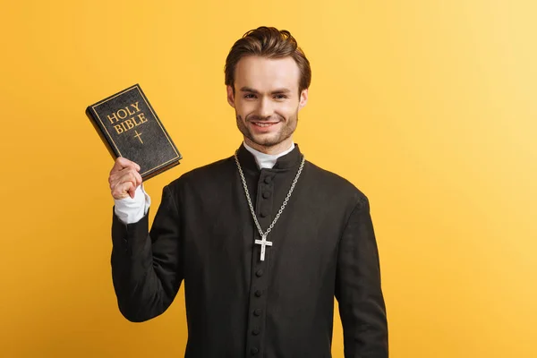 Happy Catholic Priest Holding Bible While Smiling Camera Isolated Yellow — Stok fotoğraf