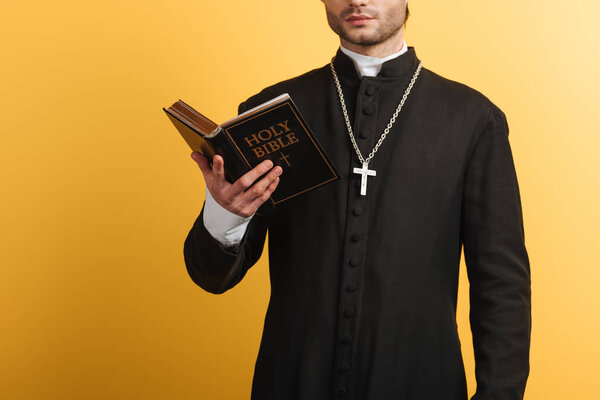 cropped view of catholic priest reading bible isolated on yellow