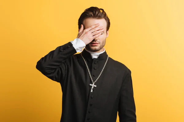 Young Catholic Priest Covering Eyes Hand Isolated Yellow — Stok fotoğraf