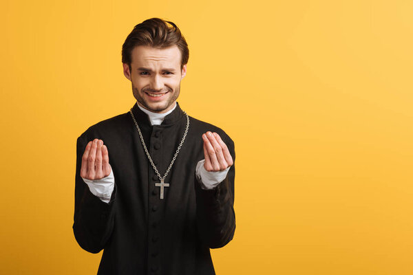 discouraged catholic priest showing question gesture isolated on yellow