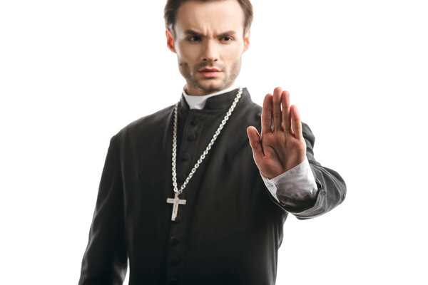 selective focus of serious, strict catholic priest showing stop gesture isolated on white