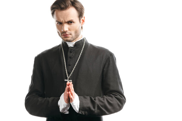 serious, strict catholic priest with praying hands looking at camera isolated on white