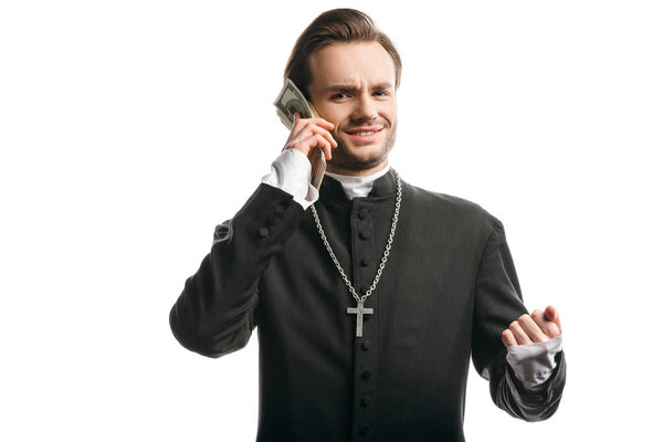 corrupt catholic priest looking at camera while holding money near head isolated on white