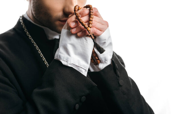 partial view of catholic priest praying while holding wooden rosary beads near face isolated on white
