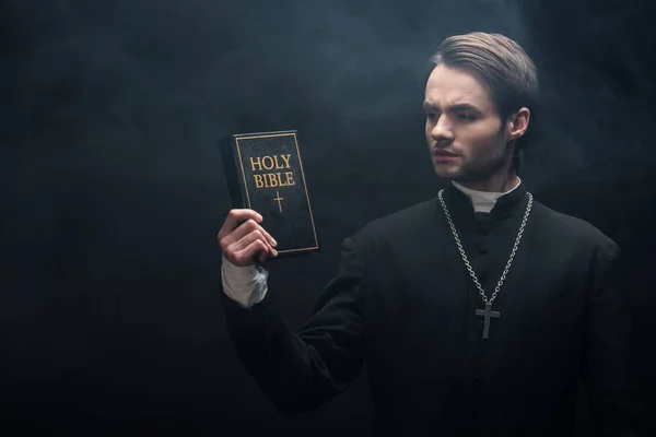 Padre Católico Pensativo Olhando Para Bíblia Sagrada Fundo Preto Com — Fotografia de Stock