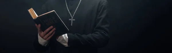 黒いパノラマのショットに隔離された聖書を読むカトリック聖職者の部分的な見解 — ストック写真