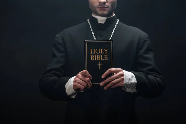 Vista Recortada Del Sacerdote Católico Sosteniendo Sagrada Biblia Aislada Negro — Foto de Stock