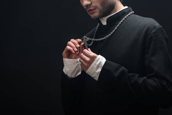 обрезанный вид католического священника, смотрящего на серебряный крест на своем ожерелье, изолированном от черного
