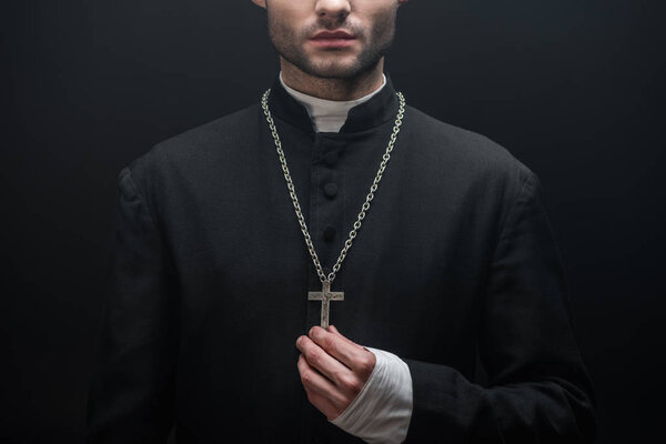 cropped view of catholic priest touching silver cross isolated on black